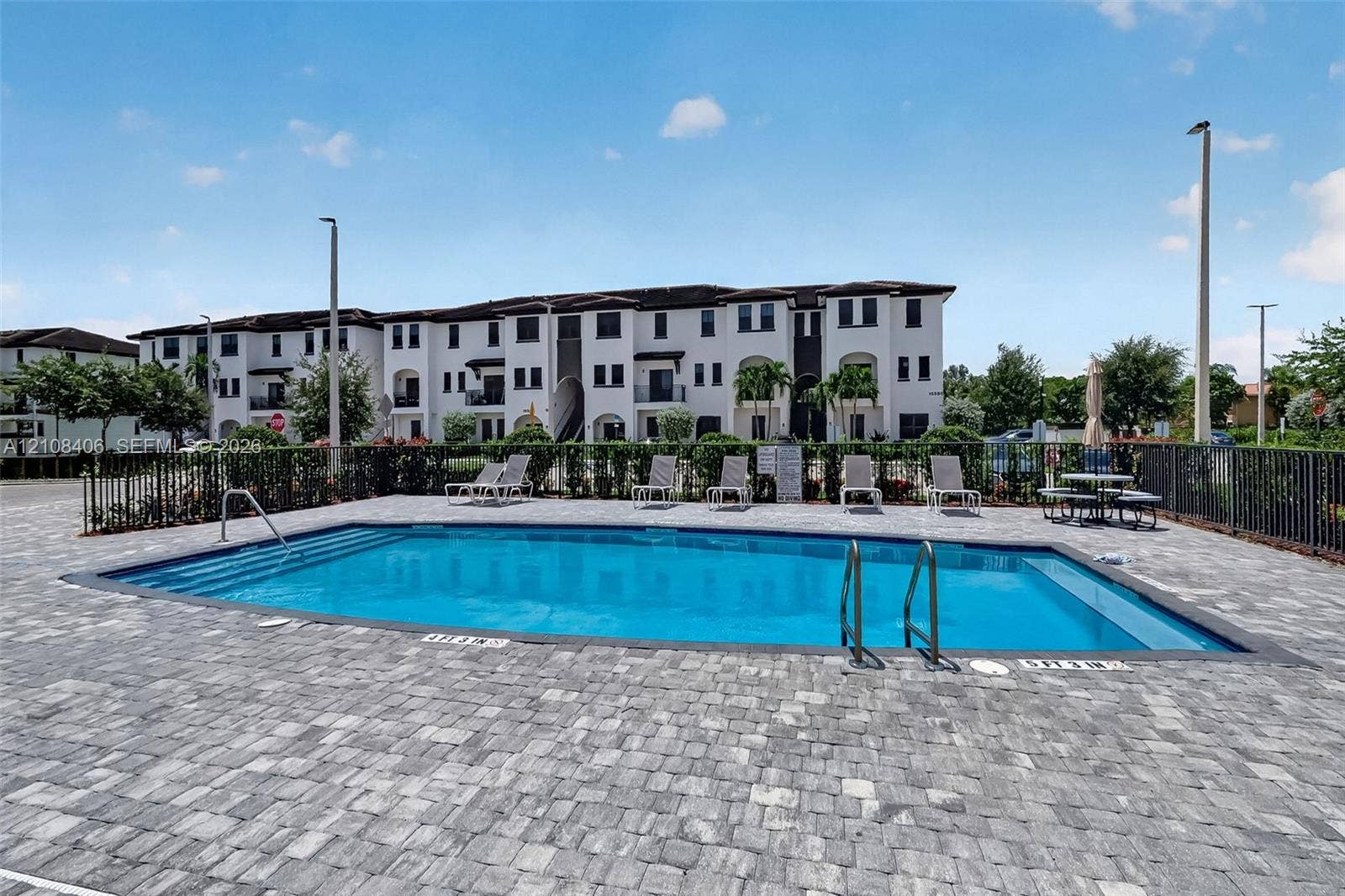15650 SW 136th Street, #212, Miami, FL 33196 Rectangular swimming pool featuring integrated steps and a paved stone deck, enclosed by perimeter metal fencing