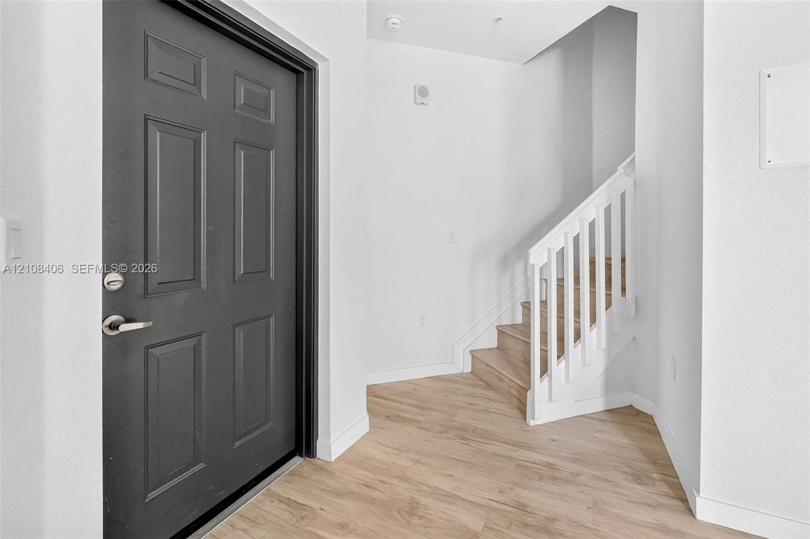 15650 SW 136th Street, #212, Miami, FL 33196 Entryway featuring a dark-finish paneled door, wood-finish flooring, and a staircase with white balusters and wood-finish treads
