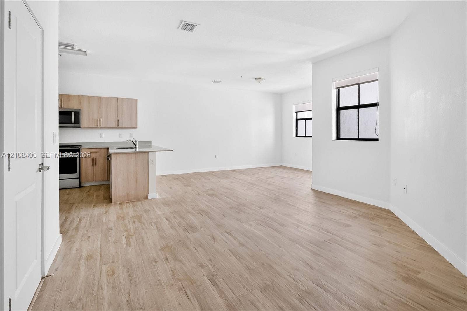 15650 SW 136th Street, #212, Miami, FL 33196 Open-concept floor plan featuring wood-finish flooring, cabinetry with a light natural finish, stainless steel appliances, and large windows with black frames