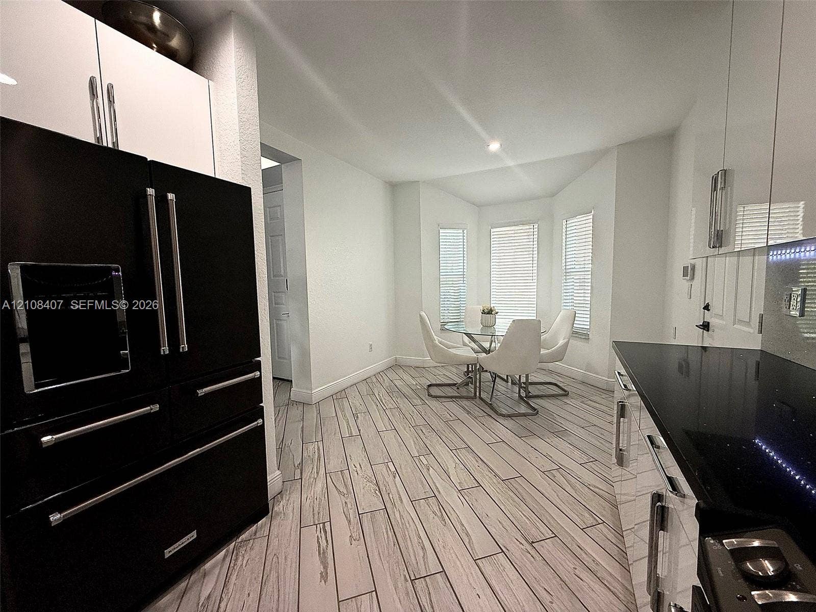 2602 Augusta Drive, #35, Homestead, Homestead, FL 33035 Modern kitchen featuring white high-gloss cabinetry, black polished countertops, a professional-style black refrigerator, and wood-finish flooring with a bay window configuration