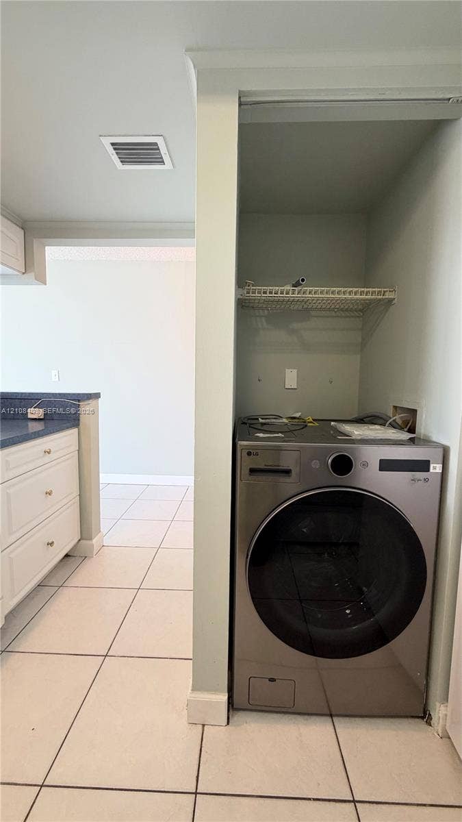 7601 E Treasure Drive, #618, North Bay Village, North Bay Village, FL 33141 Laundry alcove featuring a stainless steel front-load washer, wire shelving, and neutral floor tile