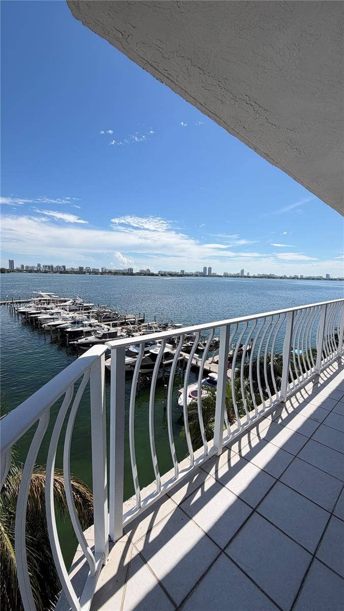 7601 E Treasure Drive, #618, North Bay Village, North Bay Village, FL 33141 Covered balcony featuring white tile flooring and a decorative white metal railing, overlooking a marina and open water