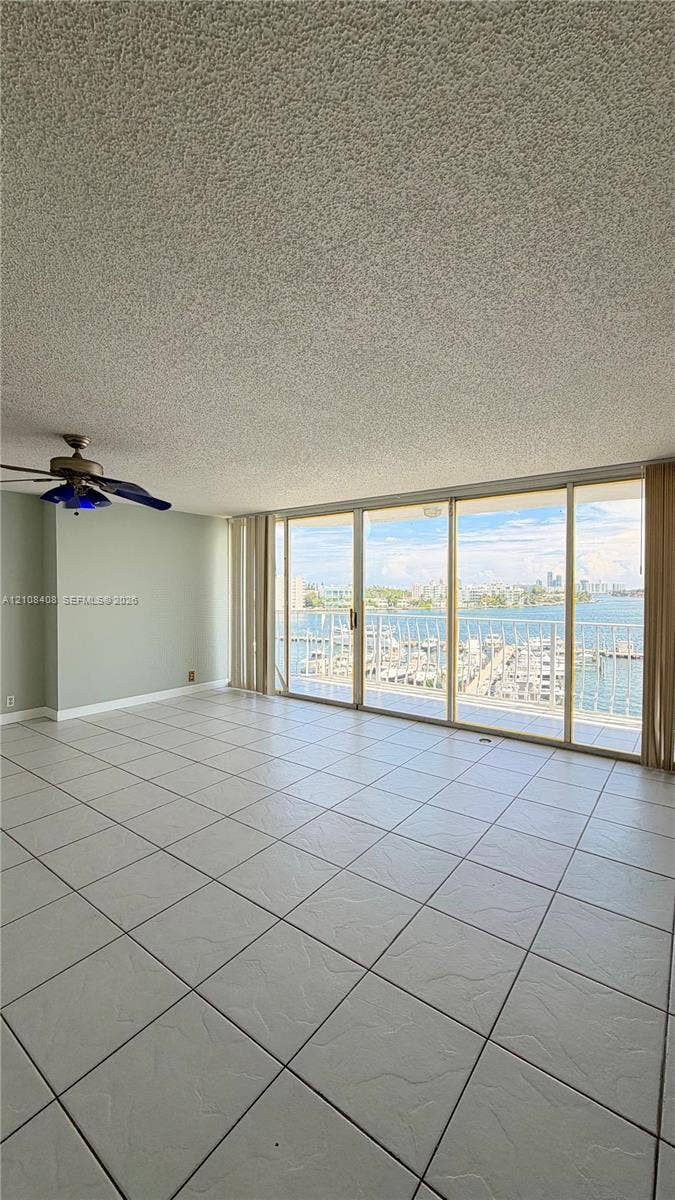 7601 E Treasure Drive, #618, North Bay Village, North Bay Village, FL 33141 Living area featuring floor-to-ceiling sliding glass doors, ceramic tile flooring, a ceiling fan, and balcony access with water and marina scenery