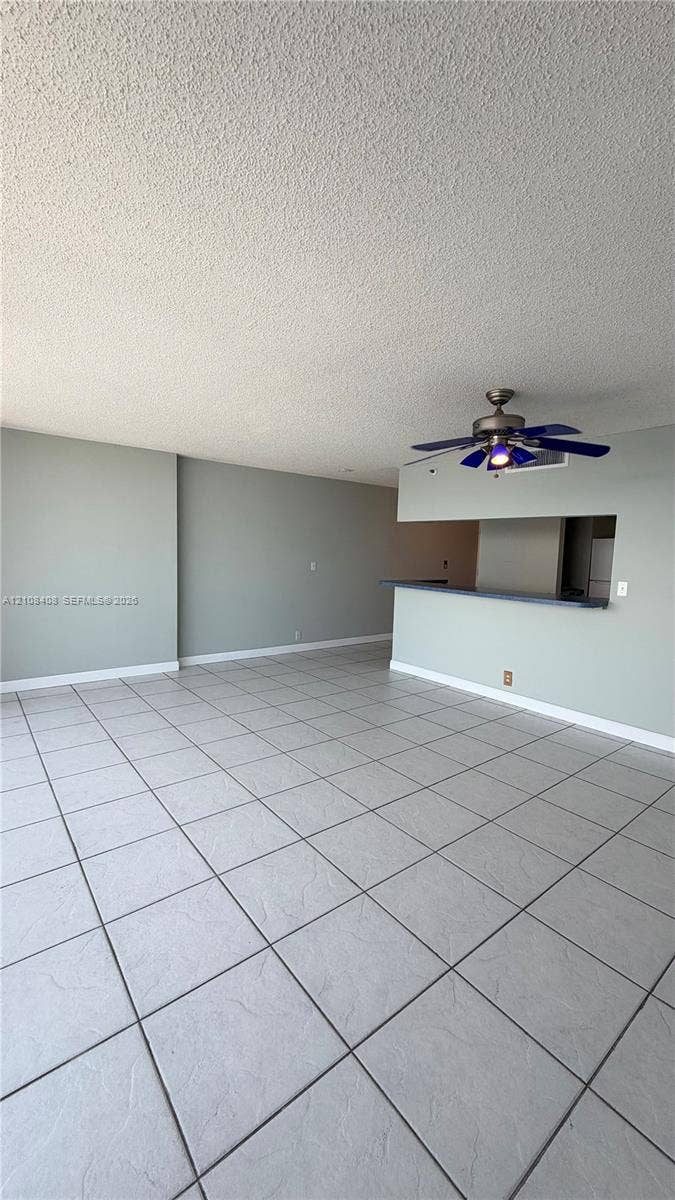 7601 E Treasure Drive, #618, North Bay Village, North Bay Village, FL 33141 Large-format ceramic tile flooring, neutral wall tones, and a peninsula-style breakfast bar featuring a pass-through counter and a multi-blade ceiling fan with integrated lighting