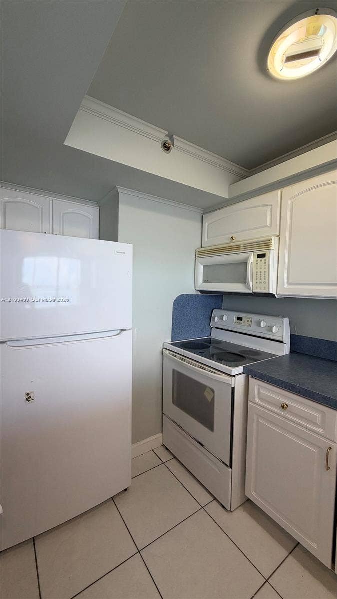 7601 E Treasure Drive, #618, North Bay Village, North Bay Village, FL 33141 Kitchen featuring white cabinetry, solid-surface countertops, tile flooring, and built-in appliances including a refrigerator, electric range, and over-the-range microwave