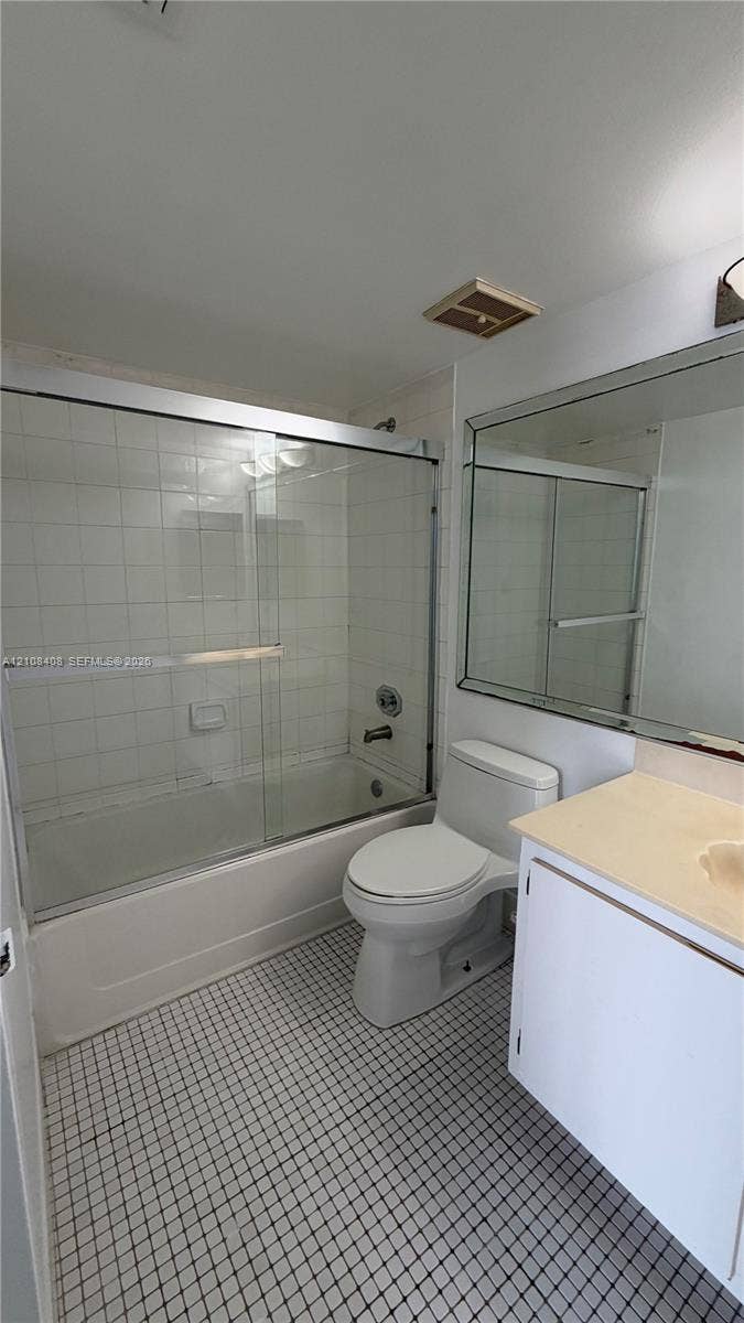 7601 E Treasure Drive, #618, North Bay Village, North Bay Village, FL 33141 Bathroom featuring a combination bathtub and shower with a glass sliding enclosure, white tiled tub surround, vanity with a solid-surface countertop, and a large wall-mounted mirror
