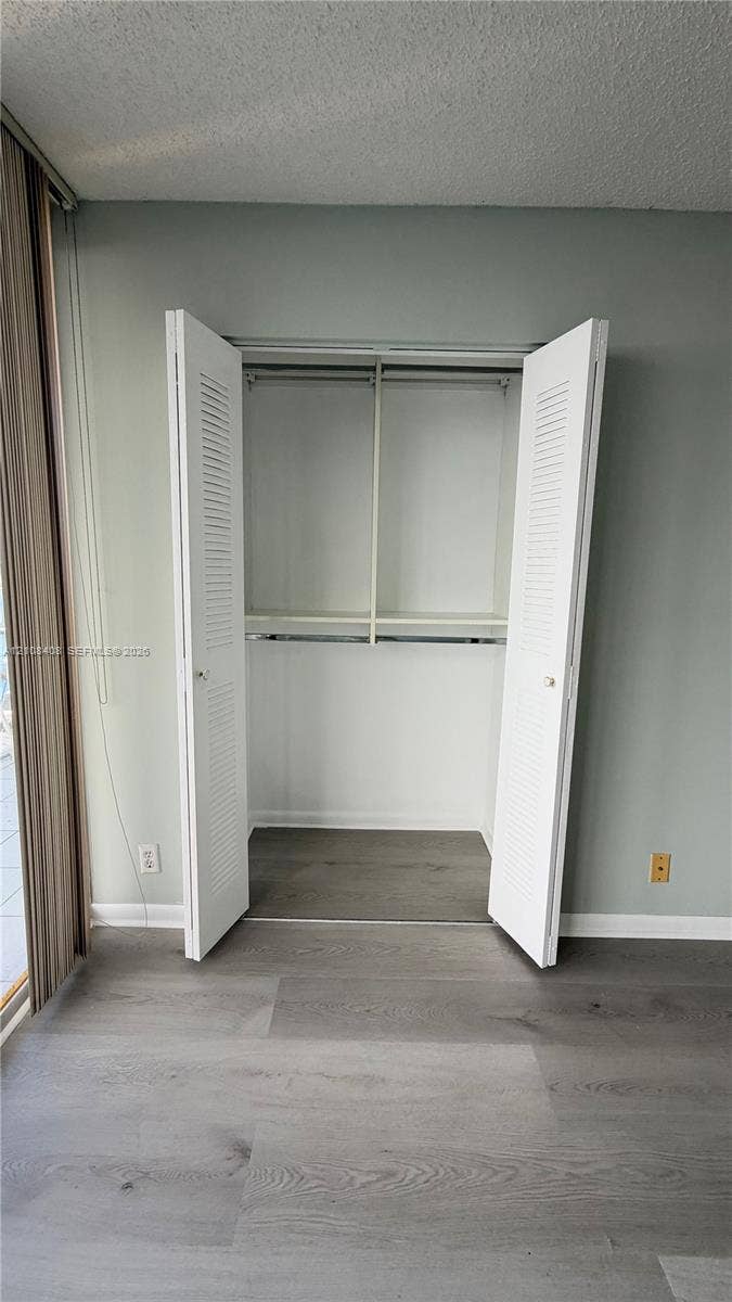 7601 E Treasure Drive, #618, North Bay Village, North Bay Village, FL 33141 Closet featuring white louvered bifold doors, integrated shelving, and metal hanging rods, complemented by wood-finish flooring