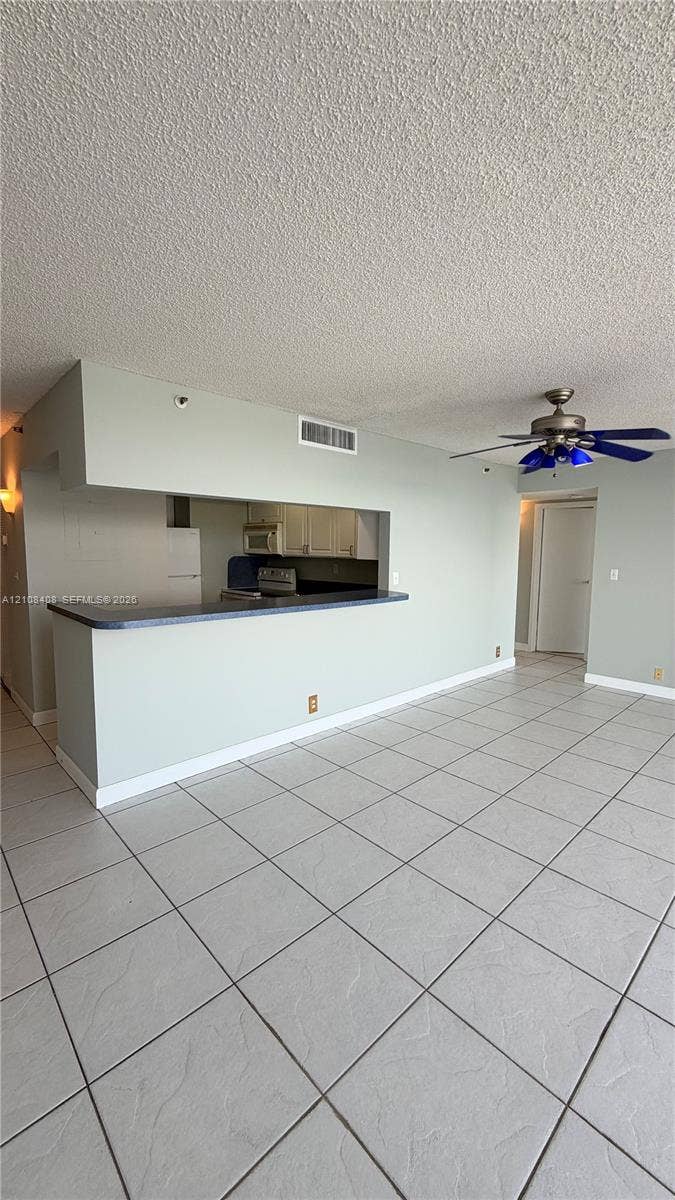 7601 E Treasure Drive, #618, North Bay Village, North Bay Village, FL 33141 Open-concept interior featuring large-format tile flooring, a breakfast bar with dark surfacing, a ceiling fan, and built-in cabinetry