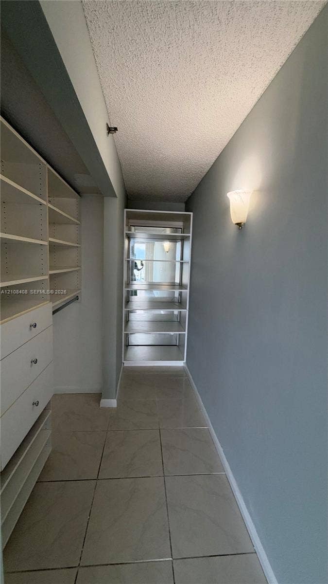 7601 E Treasure Drive, #618, North Bay Village, North Bay Village, FL 33141 Walk-in closet featuring white built-in shelving, integrated storage drawers with silver-tone hardware, tile flooring, and a wall-mounted sconce