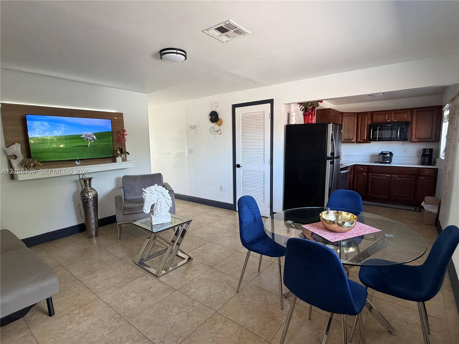 Tile flooring, kitchen featuring dark wood cabinetry, built-in television mount with accent lighting, and louvered door