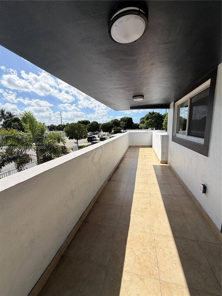 Covered balcony featuring tile flooring, smooth stucco walls, and ceiling-mounted light fixtures