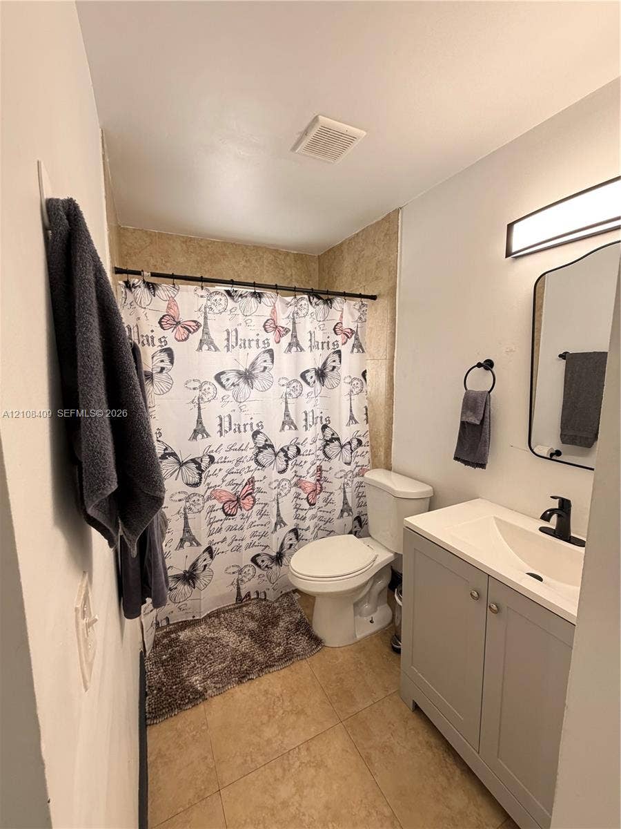 Bathroom featuring a grey vanity with a white integrated basin, matte black faucet, tile flooring, and a wall-mounted light fixture
