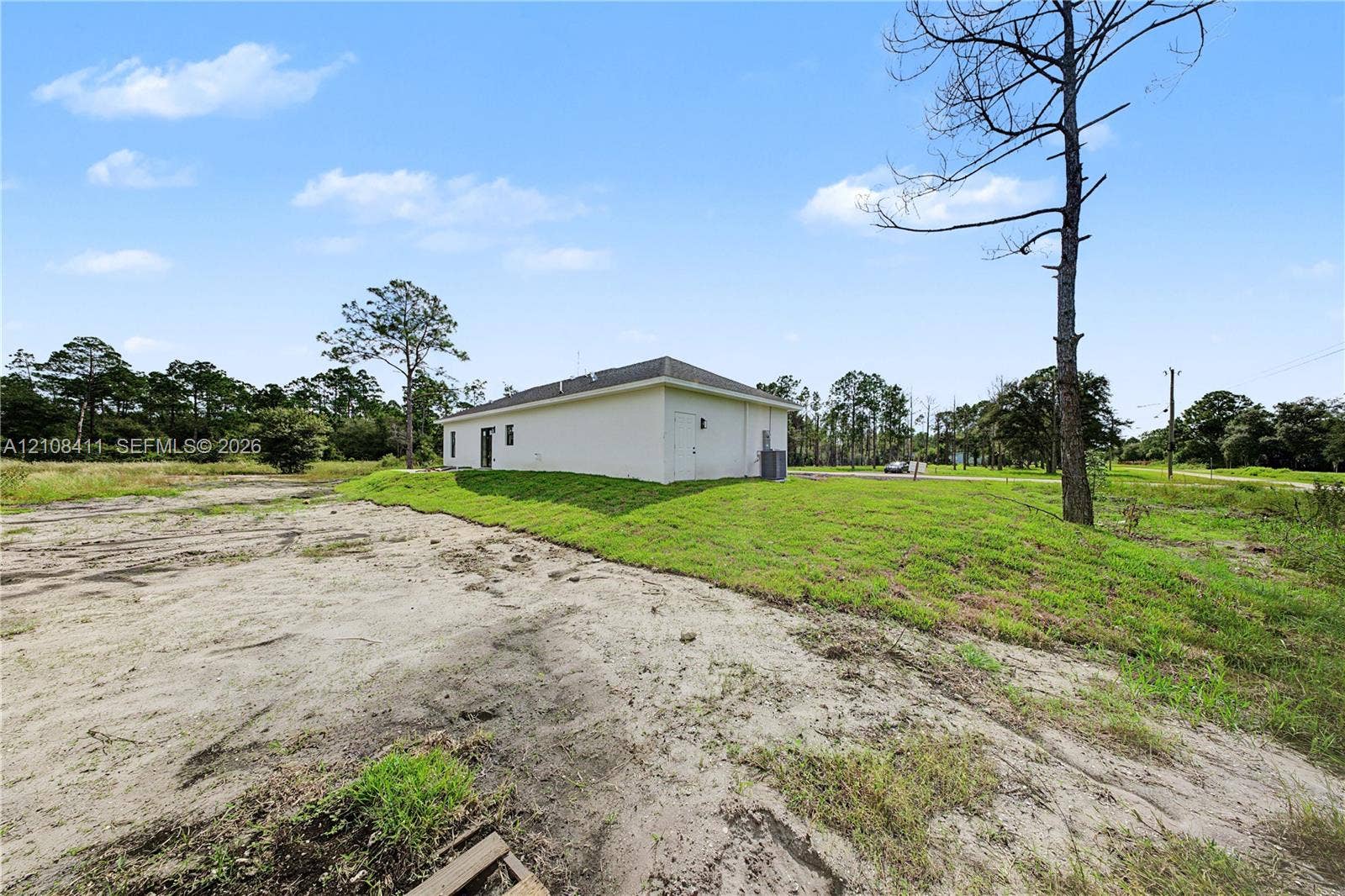 527 Avenida Del Sur, Clewiston, FL 33440 White exterior siding, hipped roofline, and expansive grounds featuring natural vegetation