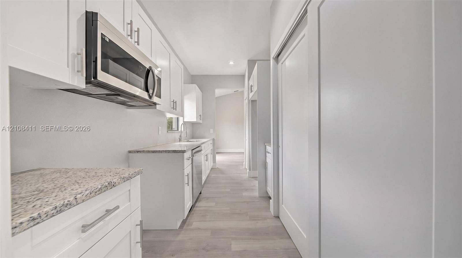 527 Avenida Del Sur, Clewiston, FL 33440 White shaker-style cabinetry featuring satin nickel hardware, speckled stone-finish countertops, stainless steel over-the-range microwave, built-in dishwasher, and wood-finish flooring