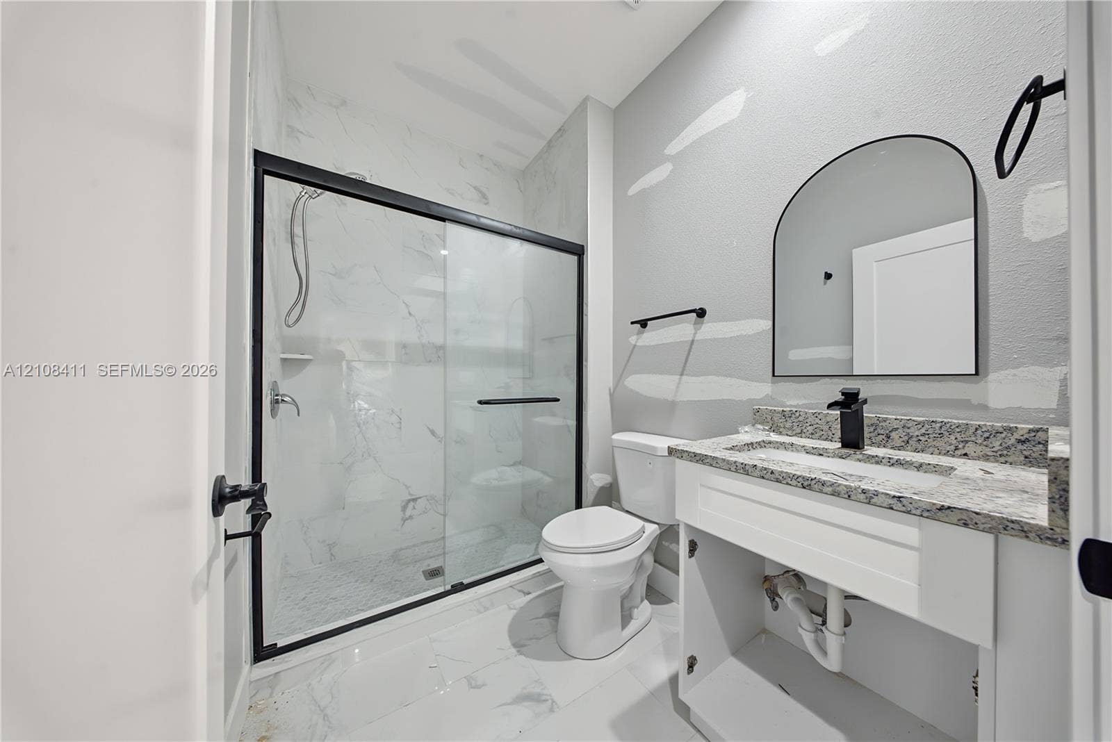 527 Avenida Del Sur, Clewiston, FL 33440 Bathroom featuring a walk-in shower with glass enclosure, stone-finish vanity countertop, arched wall mirror, and matte black hardware