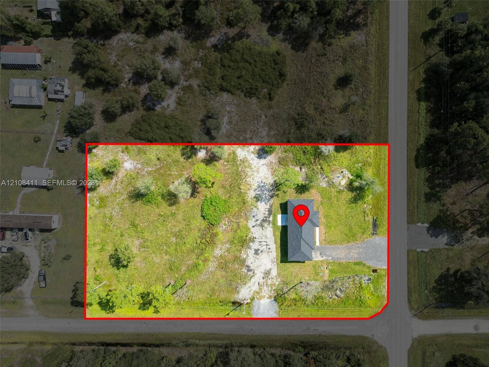 527 Avenida Del Sur, Clewiston, FL 33440 Aerial view of a corner lot featuring a detached structure, gravel driveway, mature trees, and expansive open green space