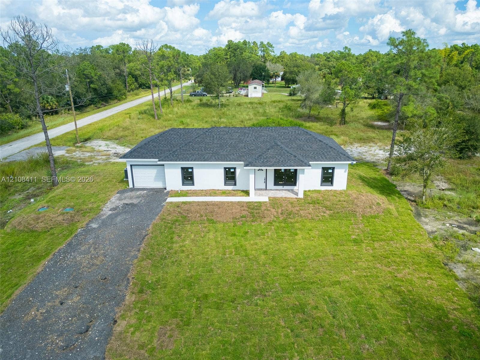 527 Avenida Del Sur, Clewiston, FL 33440 Single-story exterior featuring white stucco siding, a dark shingled roof, contrasting black window frames, and a gravel driveway