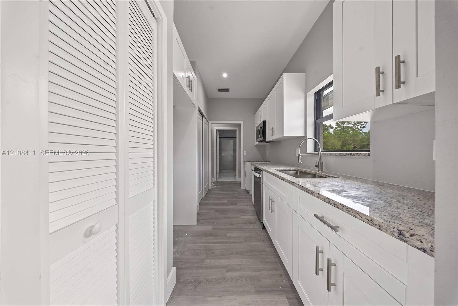 527 Avenida Del Sur, Clewiston, FL 33440 Galley kitchen featuring white Shaker-style cabinetry, stone-finish countertops, stainless steel undermount sink with a gooseneck faucet, wood-finish flooring, and white louvered-door closets