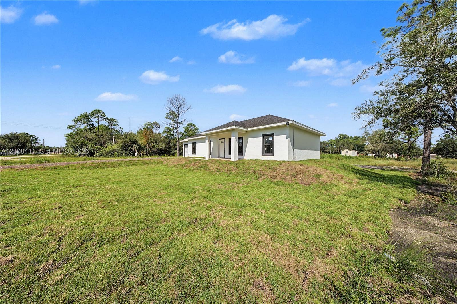 527 Avenida Del Sur, Clewiston, FL 33440 Single-story exterior featuring light-colored stucco siding, a hipped roof with dark shingles, a recessed entryway, and contrasting dark-framed windows