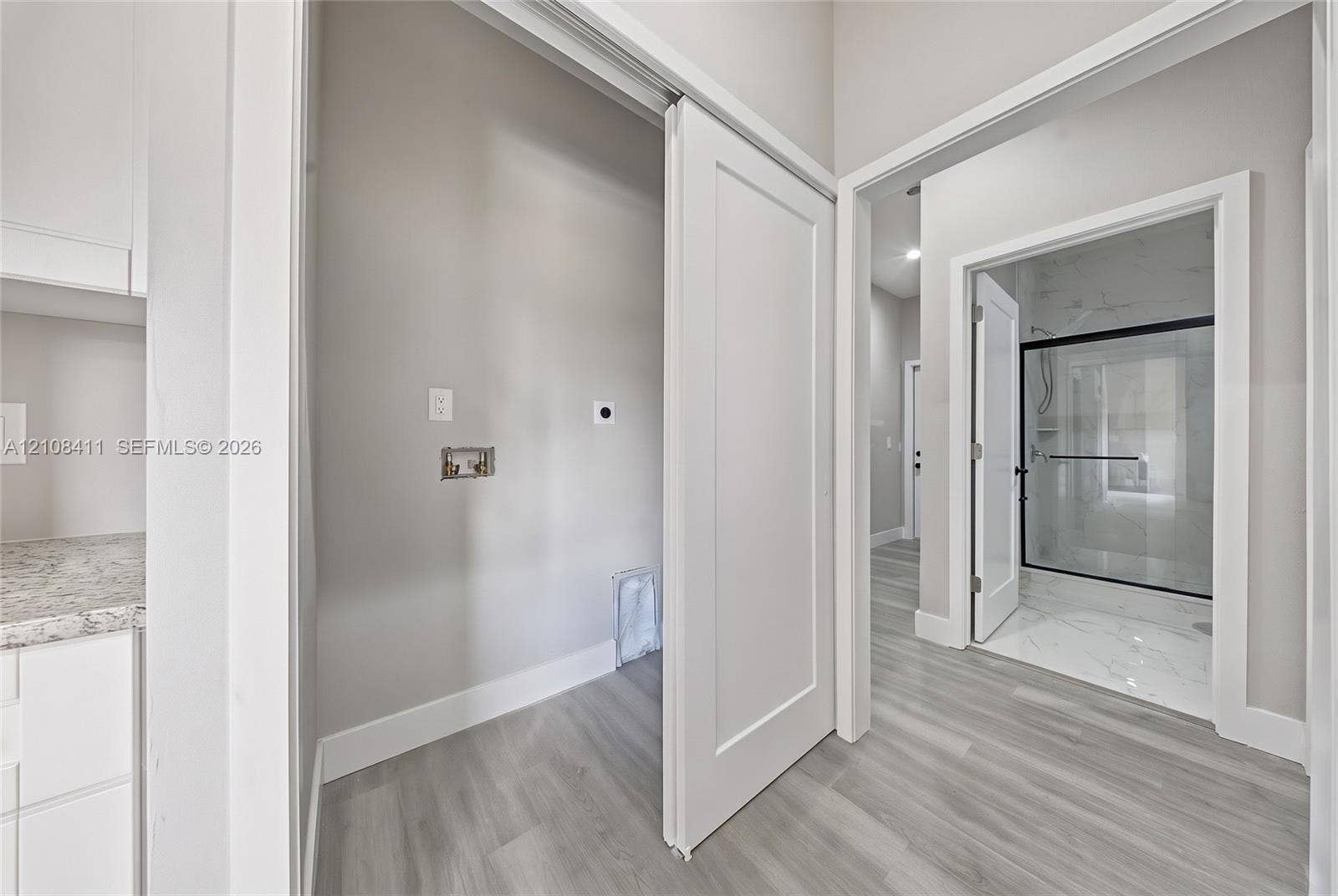 527 Avenida Del Sur, Clewiston, FL 33440 Utility space featuring light-toned wood-finish flooring, white cabinetry with speckled stone-finish countertops, and a sliding door, with a glimpse of a walk-in shower containing light-toned stone-finish tile and a black-framed glass enclosure