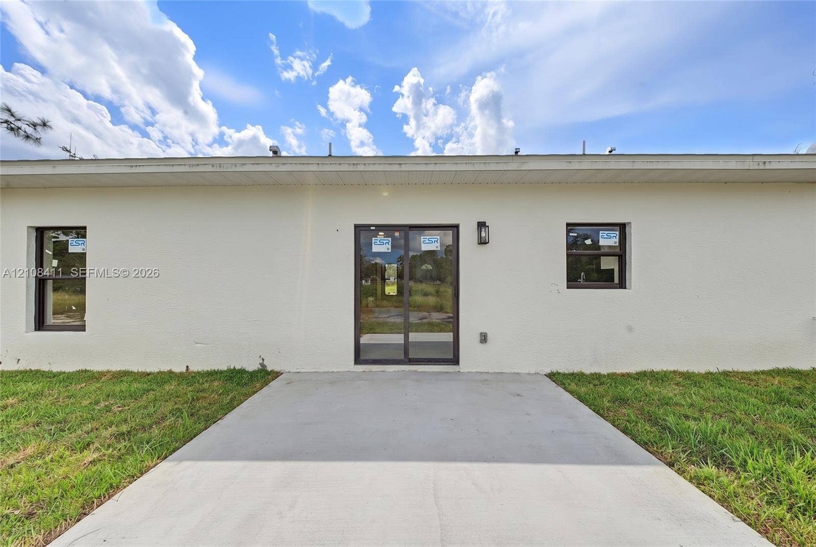 527 Avenida Del Sur, Clewiston, FL 33440 Stucco exterior finish, concrete patio, sliding glass door, and two single-pane windows with dark frames