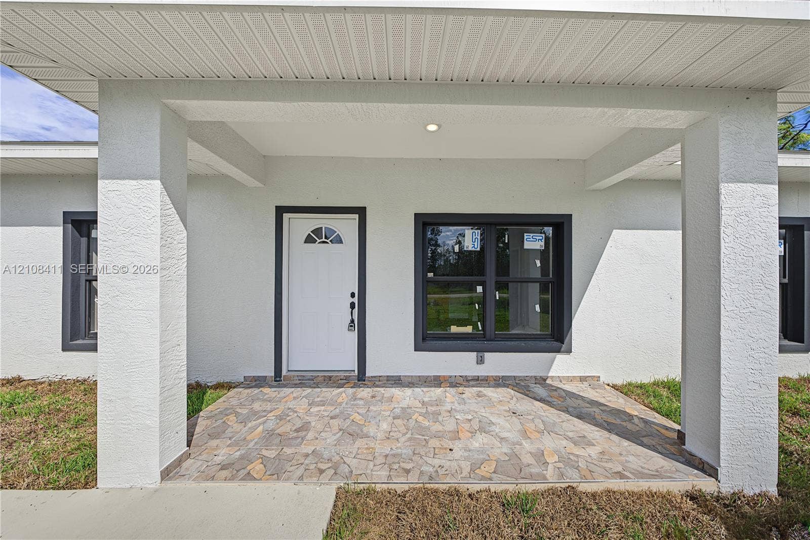 527 Avenida Del Sur, Clewiston, FL 33440 Covered entryway featuring a stone-paver porch, structural support columns, white door with a semi-circular transom window, and dark-framed windows