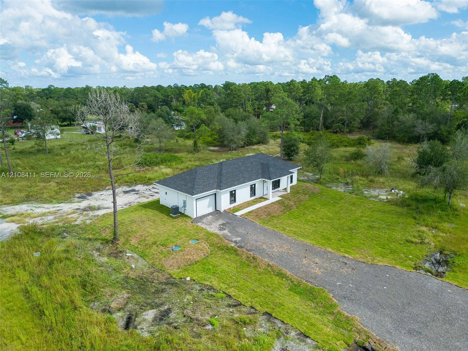527 Avenida Del Sur, Clewiston, FL 33440 Single-story residence featuring a multi-hip roof, white exterior, attached garage, and a gravel driveway situated on a cleared lot