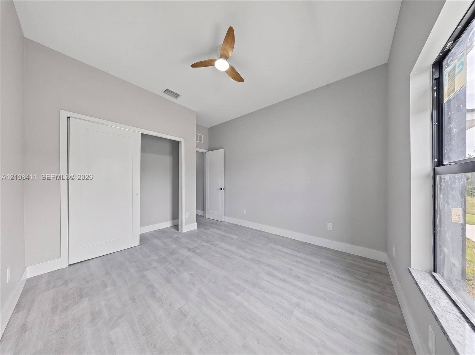 527 Avenida Del Sur, Clewiston, FL 33440 Neutral-toned interior featuring wood-finish flooring, a contemporary three-blade ceiling fan with integrated lighting, sliding closet doors, and a large window with a stone-finish sill
