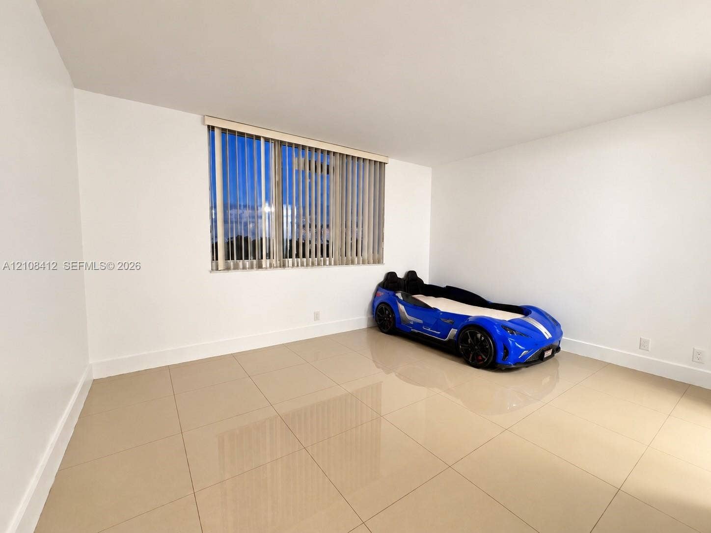 Neutral-toned tile flooring, smooth white wall finishes, and a large window featuring vertical blinds