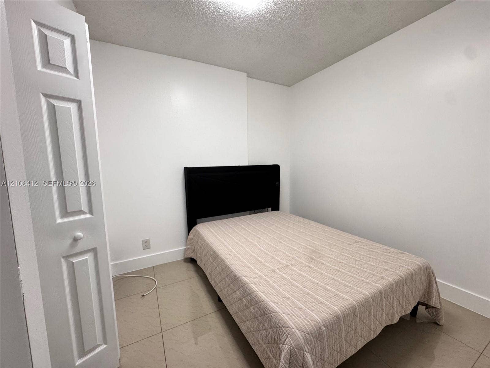 Neutral interior featuring large-format ceramic tile flooring, bright white walls, and a multi-panel bi-fold closet door
