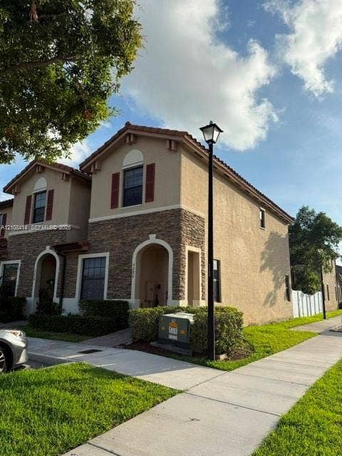 Two-story exterior featuring a stucco facade, stone veneer accents, arched entryway, and louvered shutters