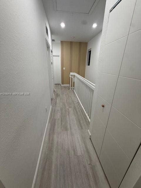 Hallway featuring wood-finish flooring, white paneled doors, recessed ceiling lighting, and a white baluster railing