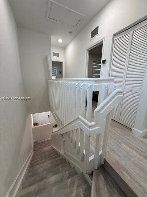 Staircase featuring a white wood balustrade and handrail, paired with light-toned wood-finish flooring and louvered bifold closet doors
