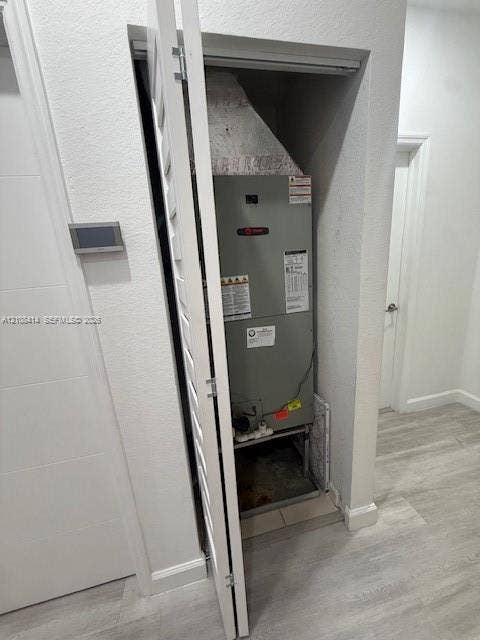 Utility closet housing a HVAC unit with louvered bi-fold door, wall-mounted digital thermostat, and wood-finish flooring