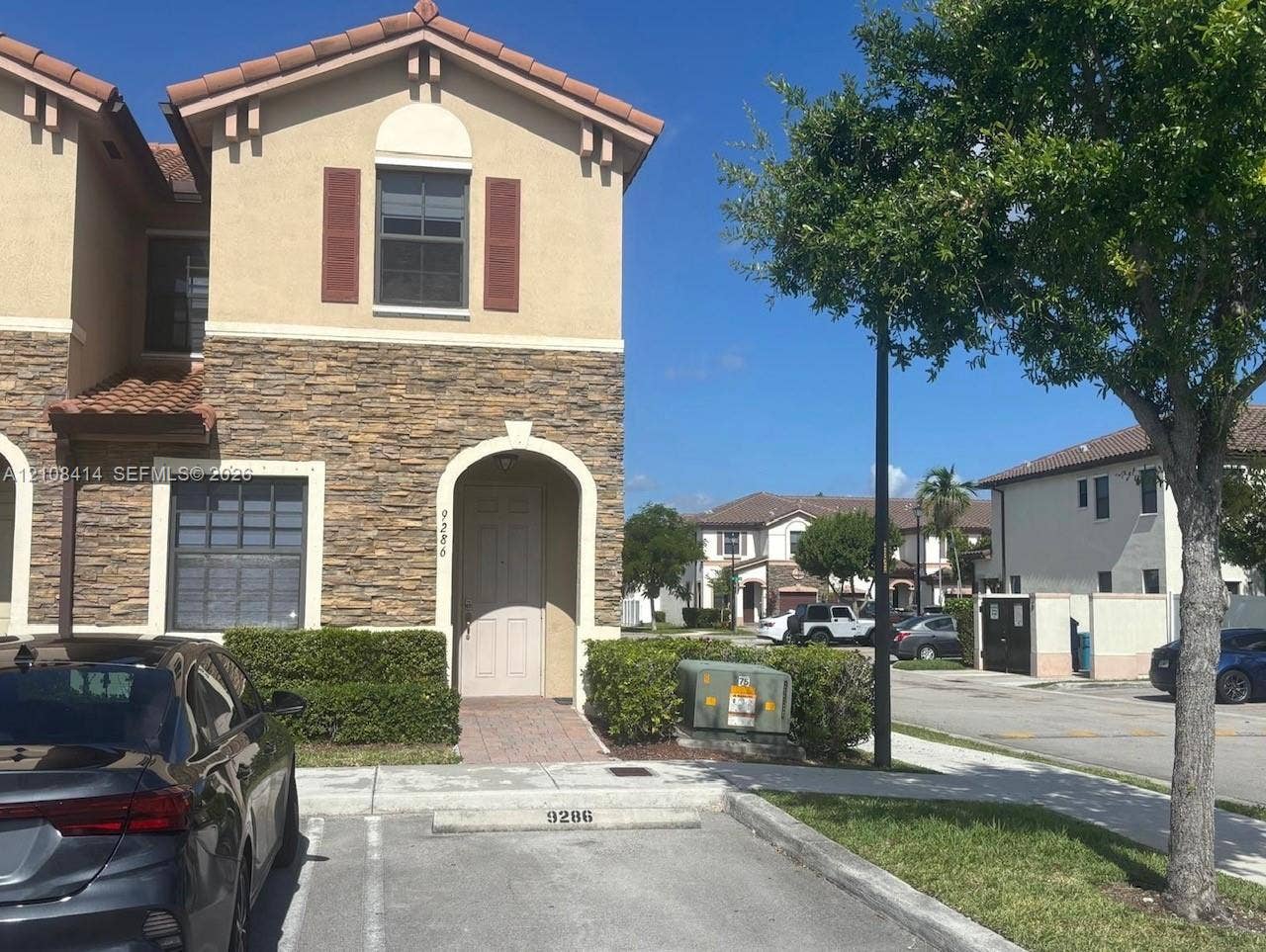 Multi-level exterior featuring tan stucco siding, stone veneer accents, arched entryway, and clay-tile roofing