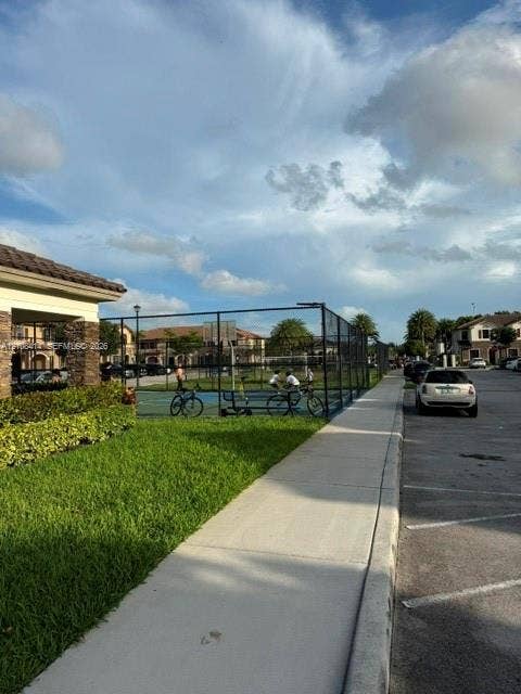 Fenced athletic court with blue surfacing, manicured lawn, and paved walkways