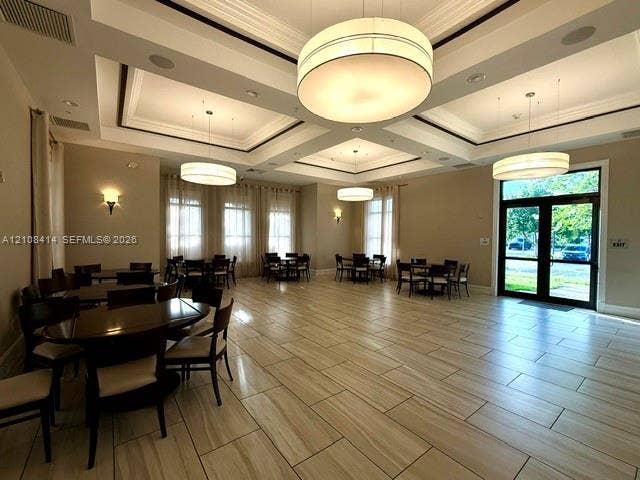 Expansive multipurpose room featuring high coffered ceilings, large drum-style pendant lighting, tile flooring, and floor-to-ceiling windows
