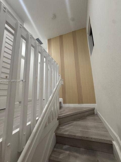 Staircase featuring wood-finish treads, a white balustrade, and a decorative light wood panel accent wall with vertical slat detailing