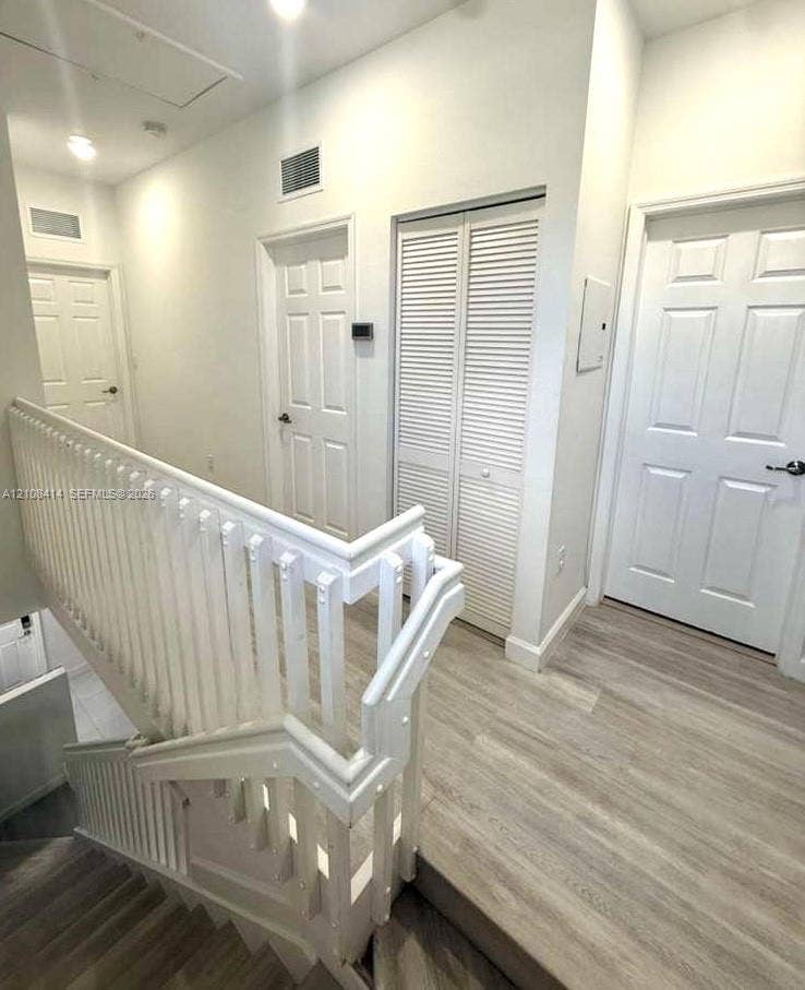 Hallway featuring wood-finish flooring, white paneled doors, louvered closet doors, and a white staircase railing