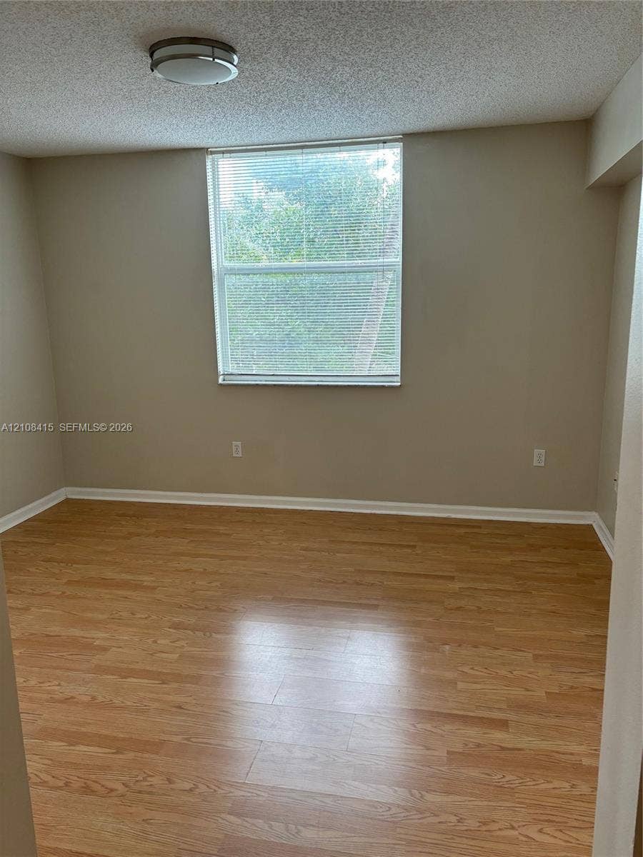 1900 Van Buren Street, #303B, Hollywood, Hollywood, FL 33020 Neutral-toned walls, wood-finish flooring, and a single-pane window with horizontal blinds and integrated flush-mount lighting