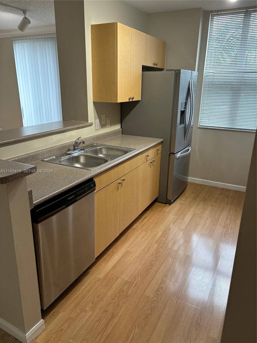 1900 Van Buren Street, #303B, Hollywood, Hollywood, FL 33020 Kitchen featuring light wood-finish cabinetry, stainless steel appliances, speckled solid-surface countertops, a double-basin stainless steel sink, and wood-finish flooring