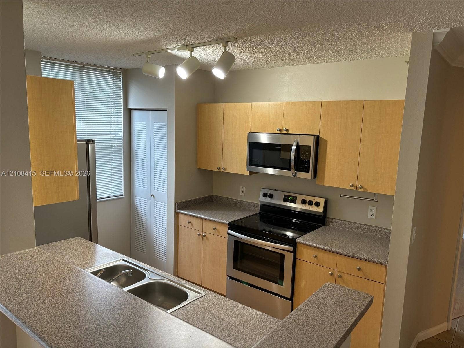 1900 Van Buren Street, #303B, Hollywood, Hollywood, FL 33020 Kitchen featuring light-tone flat-panel cabinetry, stone-composite countertops, stainless steel appliances, double-basin drop-in sink, and adjustable track lighting