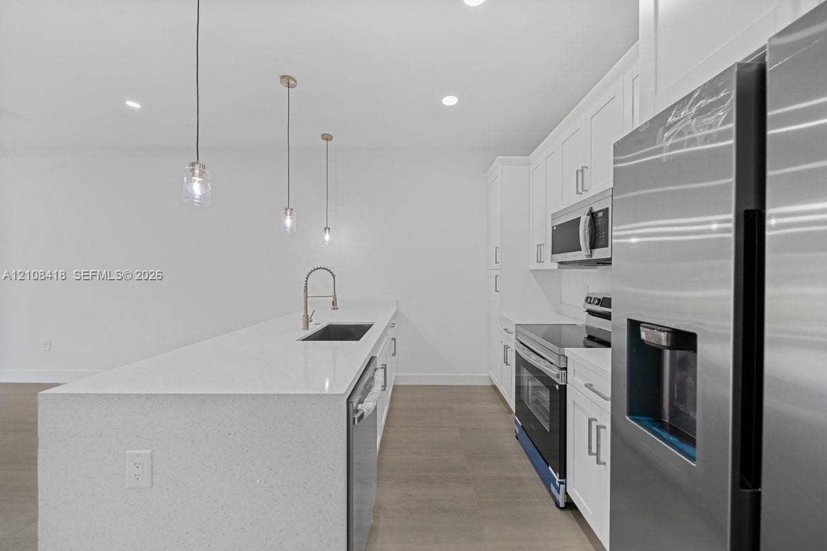 2235 Wayne Avenue S, Lehigh Acres, FL 33973 Kitchen featuring white shaker-style cabinetry, quartz countertops, an island with an undermount sink, stainless steel appliances, and wood-finish flooring