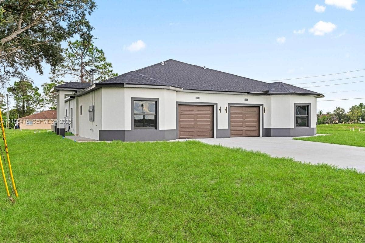 2235 Wayne Avenue S, Lehigh Acres, FL 33973 Stucco exterior featuring dual-bay garage doors, a concrete driveway, multi-faceted roofline, and trimmed windows