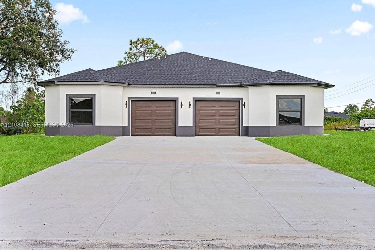 2235 Wayne Avenue S, Lehigh Acres, FL 33973 Stucco exterior with contrasting trim, dual garages, asphalt shingle roof, and a paved concrete driveway