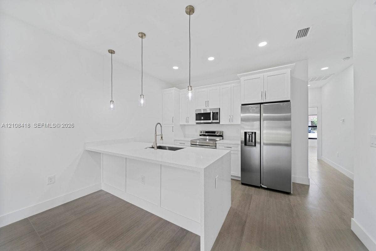2235 Wayne Avenue S, Lehigh Acres, FL 33973 Kitchen featuring white cabinetry, quartz countertops, a central island with a stainless steel sink, stainless steel appliances, and wood-finish flooring