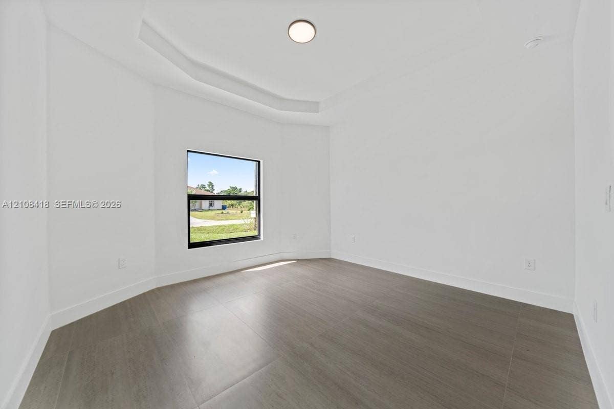 2235 Wayne Avenue S, Lehigh Acres, FL 33973 Interior space featuring tray ceilings, wood-finish tile flooring, and a single-pane window with dark trim