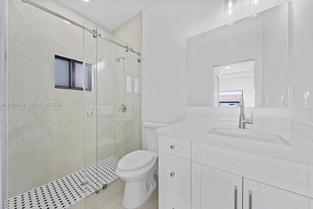 2235 Wayne Avenue S, Lehigh Acres, FL 33973 Walk-in shower featuring a glass enclosure, large-format tile surround, and black-and-white mosaic floor tiling, complemented by a white vanity with a quartz countertop and a rectangular undermount sink