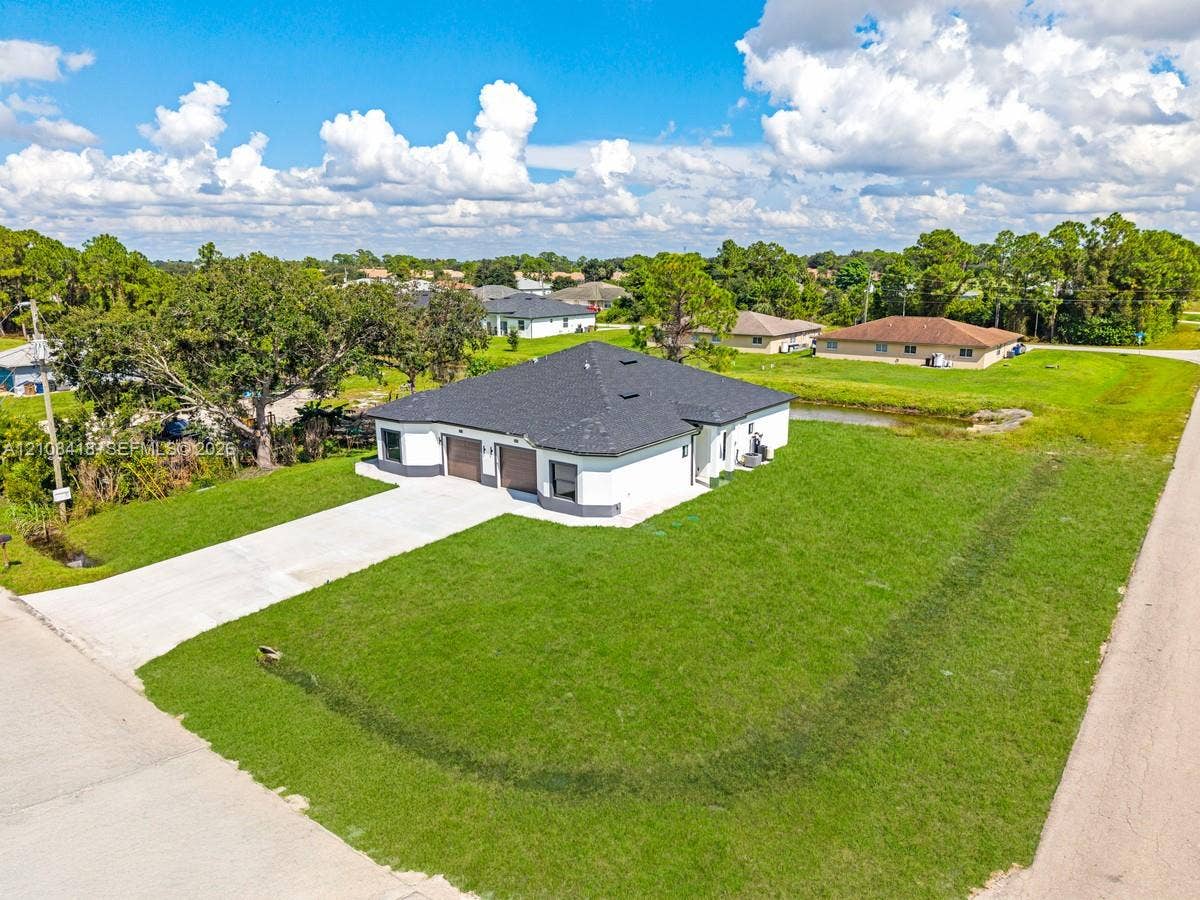 2235 Wayne Avenue S, Lehigh Acres, FL 33973 Single-story residence featuring a hipped roof, attached two-car garage, concrete driveway, and expansive lawn area