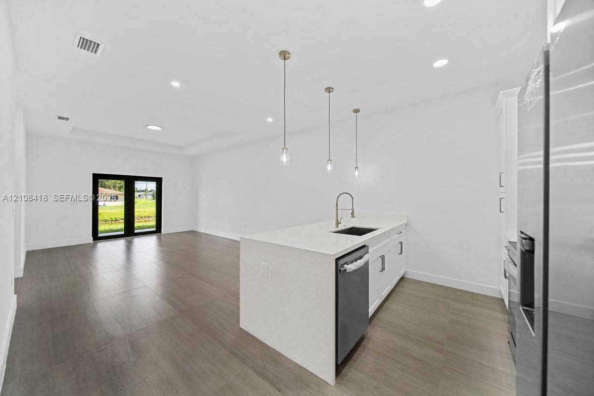 2235 Wayne Avenue S, Lehigh Acres, FL 33973 Kitchen featuring a waterfall-edge quartz island, stainless steel undermount sink, pendant lighting, wood-finish flooring, and black-framed French doors